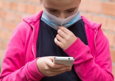 Tıbbi maskeli kız virüs ve enfeksiyonları önlemek için cep telefonu kullanıyor