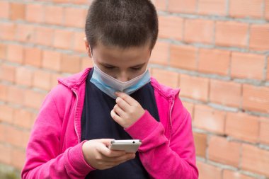 Tıbbi maskeli kız virüs ve enfeksiyonları önlemek için cep telefonu kullanıyor