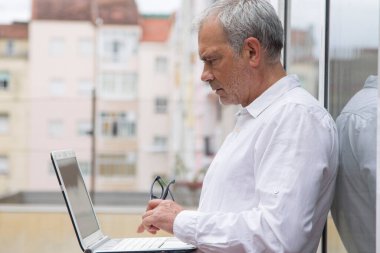 Üst düzey bir adam ofis balkonunda dizüstü bilgisayar kullanıyor.