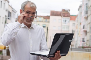 Üst düzey bir adam ofis balkonunda dizüstü bilgisayar kullanıyor.