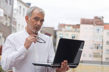 Üst düzey bir adam ofis balkonunda dizüstü bilgisayar kullanıyor.