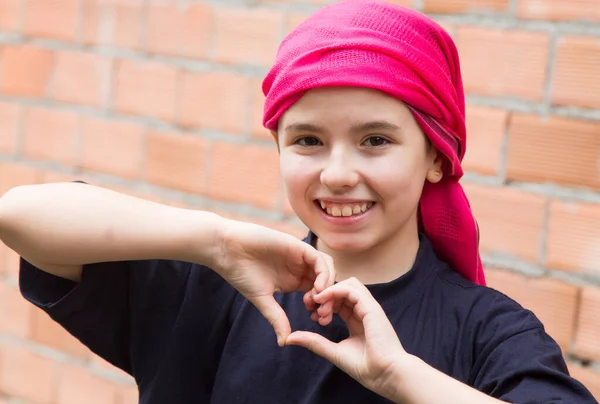 girl with a headscarf for cancer making a heart symbol with her hands