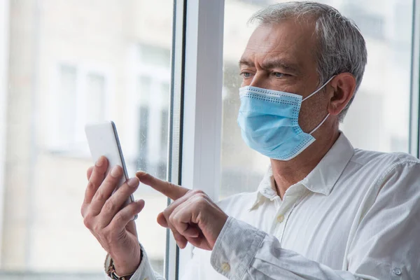 mature man with medical mask using mobile phone