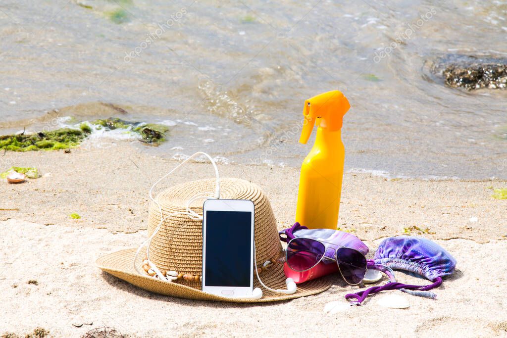 mobile phone, straw hat, suntan lotion and sunglasses on the beach promenade, summer vacation concept