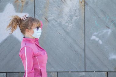 Kadın, virüslere ve enfeksiyonlara karşı korunmak için sokakta tıbbi maskeyle jimnastik yapıyor.