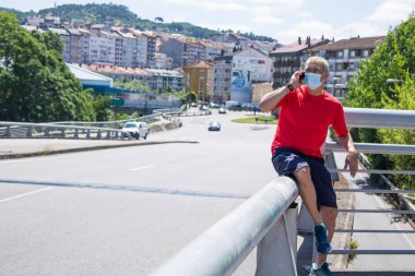 mature man with medical mask doing sports and using mobile phone in the city, concept of sport and technology in the new normal