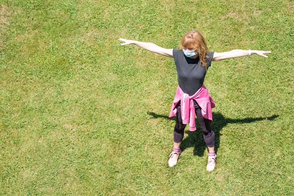 woman with medical mask doing sport exercises on the grass, new normal concept