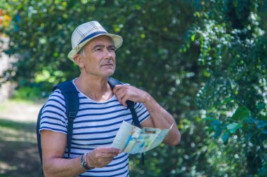 Sırt çantası ve dünya haritası olan bir turist kırsalda yürüyor.