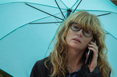 Şemsiyeli kadın cep telefonuyla konuşuyor.