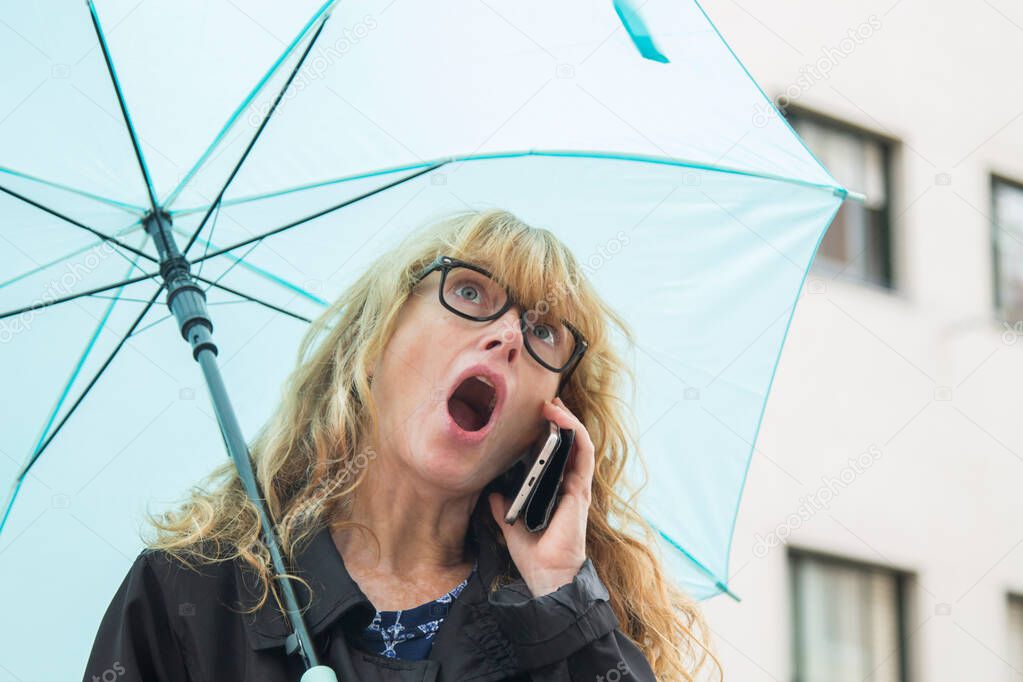 surprised woman holding umbrella and talking to the smart phone