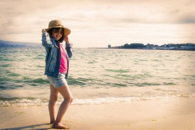 Şapkalı ve güneş gözlüklü kız sahilde yürüyor.