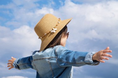 Arka planda gökyüzü ile yükselen kollarıyla özgürlük içinde oynayan küçük kız.