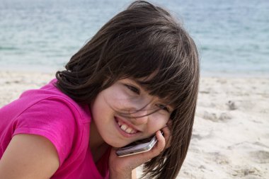 Cep telefonuyla kumda uzanan kız.