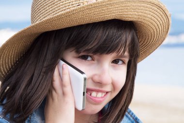 Sahilde cep telefonuyla konuşan şapkalı kız.