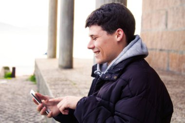 Gülümseyen adam taş duvarda akıllı telefon kullanıyor.