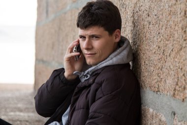  Adam cep telefonuyla konuşuyor, akranına yaslanıyor.