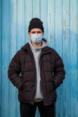 Mavi arka planda tek kullanımlık ameliyat maskesi olan bir adam.