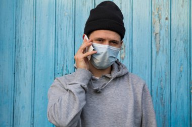 Tek kullanımlık ameliyat maskeli genç adam akıllı telefonla konuşuyor.