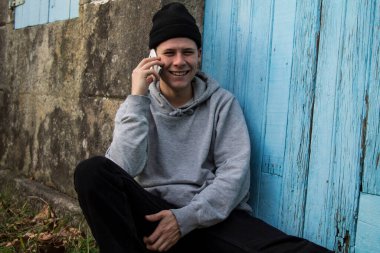 Gülümseyen adam taş duvarda akıllı telefon kullanıyor.