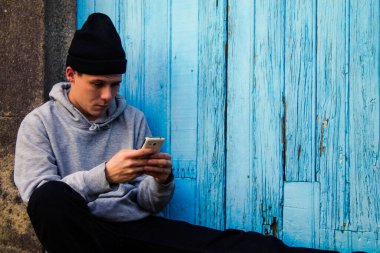Adam mavi duvarda cep telefonu kullanıyor.