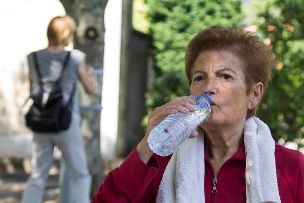 exhausted senior woman drinking after sports or exercise