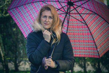 Dışarıda şemsiye tutan gülümseyen sarışın kadının portresi.