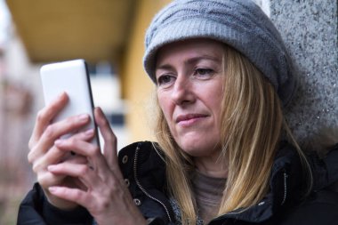 Kadın sokakta cep telefonuna bakıyor ve kontrol ediyor.