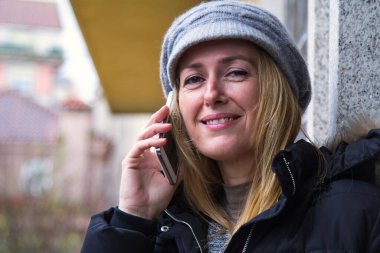 Şehirde akıllı telefon kullanan gülümseyen bir kadın.