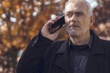 Sonbaharda cep telefonuyla konuşan olgun bir adam.