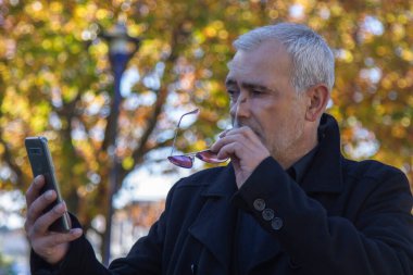 Sonbahar arkaplanı cep telefonuna bakan olgun bir adam