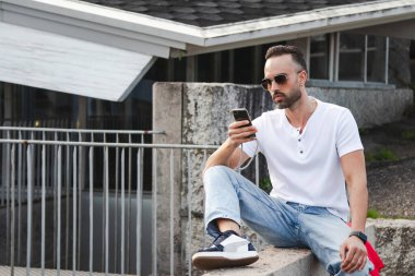 Sıradan bir genç adam sokakta oturmuş akıllı telefonunu kontrol ediyor.