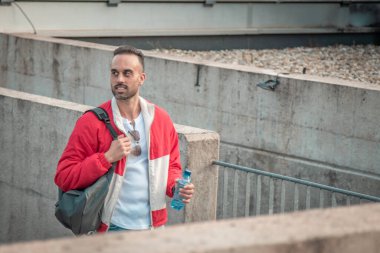 Sırt çantalı ve su şişeli genç adam şehir caddesinde