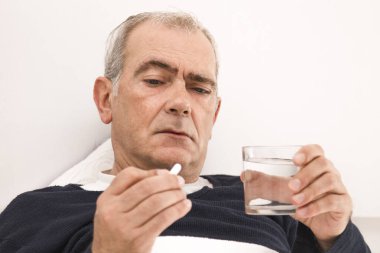 Yatakta yatan hasta kıdemli adam ilaçlarını alıyor.