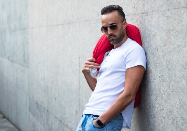 Ceketli ve güneş gözlüklü yakışıklı adam sokakta poz veriyor.