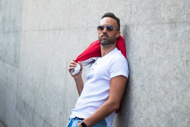 Ceket giyen yakışıklı ve güneş gözlüklü adam duvarda poz veriyor.
