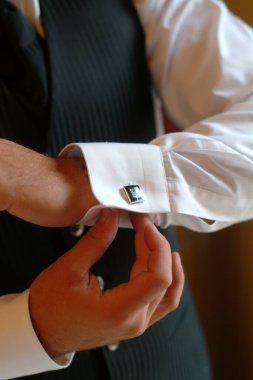 Tişörtü için kol düğmesi takan bir damadın elindeki detaylar.