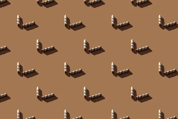 Broken wafer rolls seamless pattern with hard shadows on a brown background. Minimal sweet food concept.