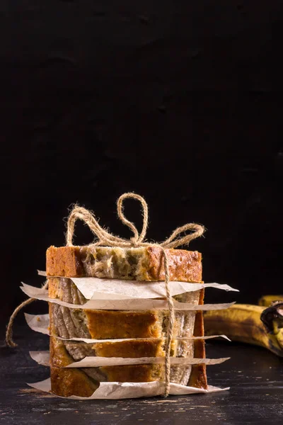 Traditional American dish - slices of banana bread between parchment on a black concrete background with copy space