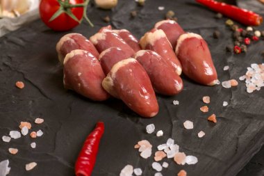 Siyah tahtada taze çiğ tavuk kalbi ve tuz. Tavuk sakatatı.