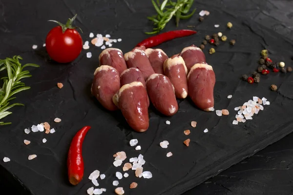 Kara tahtada taze çiğ tavuk kalbi, biber, tuz ve biberiye. Tavuk sakatatı.