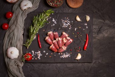 Kara tahtada taze çiğ tavuk kalbi, biber, tuz ve biberiye. Tavuk sakatatı.