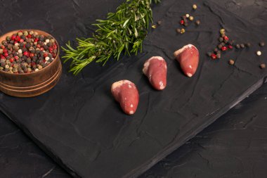 Kara tahtada taze çiğ tavuk kalbi, biber ve biberiye. Tavuk sakatatı.