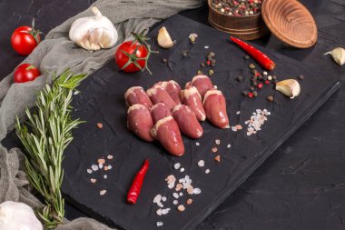 Kara tahtada taze çiğ tavuk kalbi, biber, tuz ve biberiye. Tavuk sakatatı.