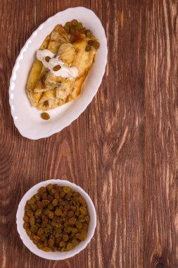 İnce dürülmüş krepler süzme peynirle doldurulmuş kuru üzümlü ve ekşi kremalı ahşap masada fotokopi alanı ile.