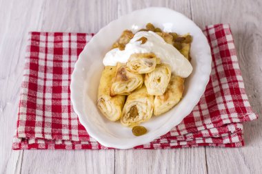 Süzme peynirli, kuru üzümlü ve beyaz ahşap masaya ekşi kremalı dürülmüş krep.