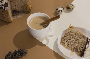 Paskalya pastası ve bıldırcın yumurtalarıyla sert bir gölgeyle kumlu bej arka planda bir fincan latte. Paskalya kartı minimalizmi. Moda izometrik bej arka plan. Yaratıcı kartpostal