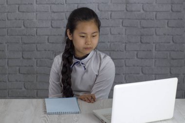 Küçük Asyalı kız çevrimiçi derste evde ders çalışıyor, çevrimiçi video konuşmayı öğreniyor. Bilgisayarlı bir okul öğretmenini dikkatle dinliyor ve evde notlar alıyor. Yeni normal. Evde kalmak..