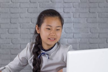 Küçük gülen Asyalı kız çevrimiçi video dersinde evde ders çalışıyor. Bilgisayarla online okul derslerine katılıyor ve evde notlar alıyor. Yeni normal. İçeride kal.