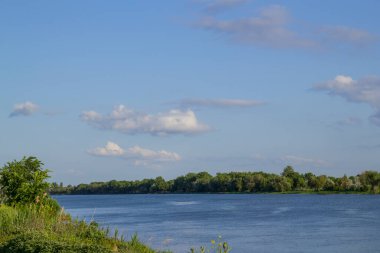 Mavi gökyüzünde beyaz pofuduk bulutlar. Güneşli bir yaz gününde nehir üzerinde.