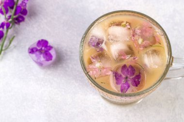 Bir bardak kapuçino, kahve ve mor çiçekli buz küpleri..